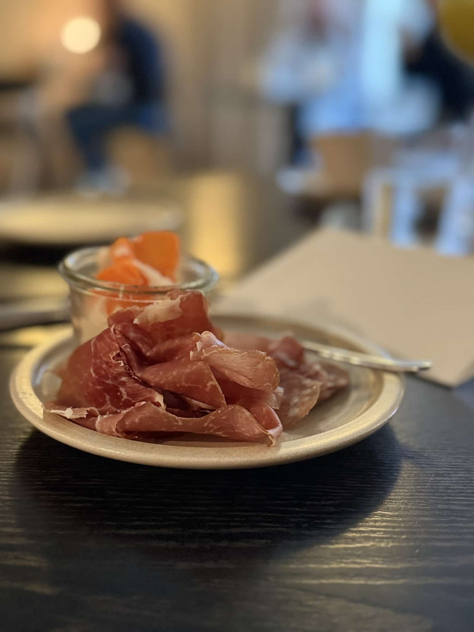 Tallerken med tyndskåret lufttørret skinke og glas med syltede grøntsager.