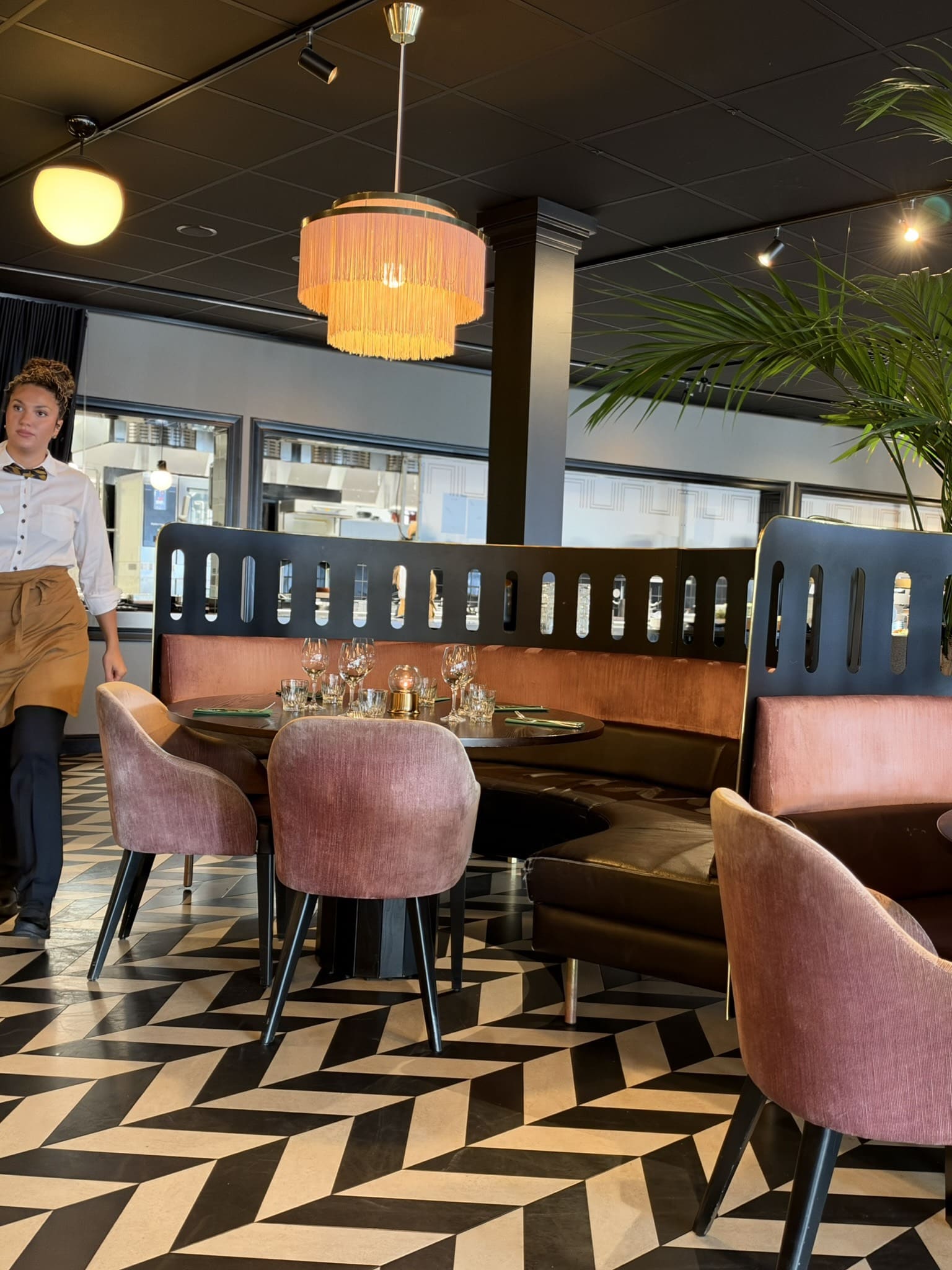Restaurantlokale med rosa stole, rund sofa, frynselampe og sort-hvidt gulv