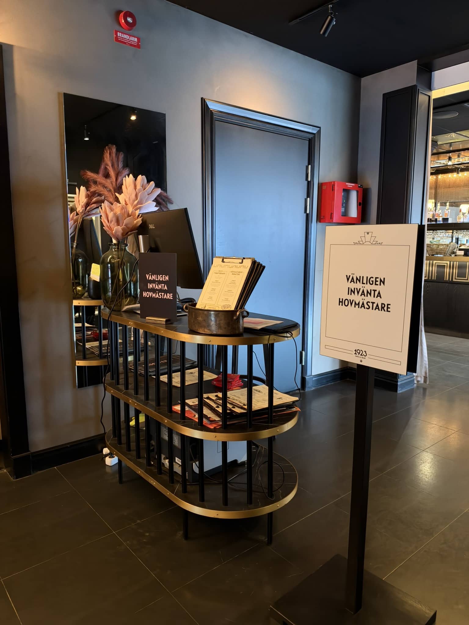 Værtsstand med skilt, menukort og tørrede blomster ved restaurantens indgang