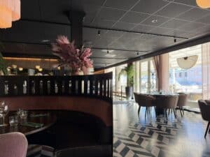 Restaurantlokale med rund rosa sofabås, mønstret gulv og borde ved vinduer