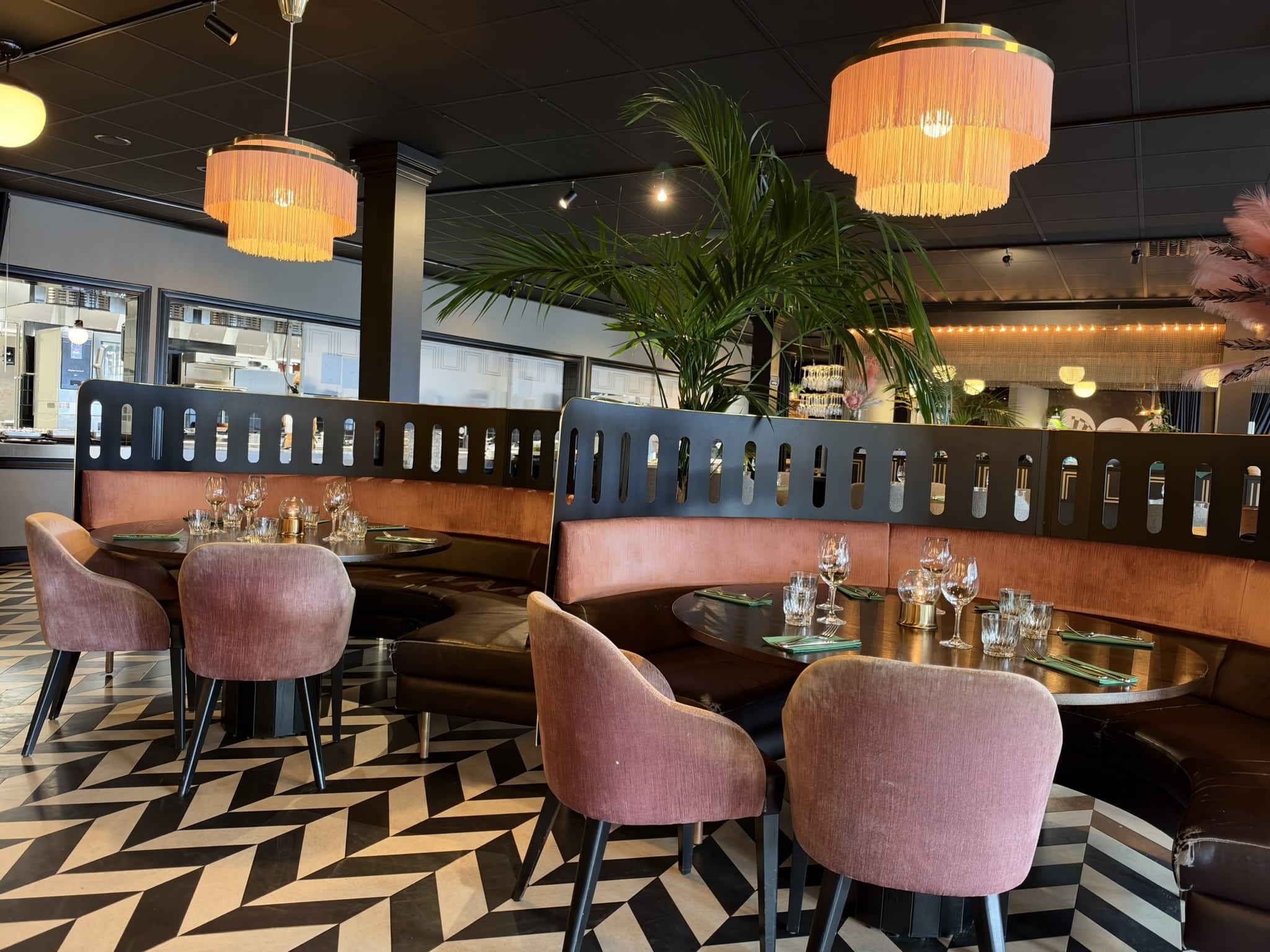 Restaurantlokale med rosa stole, runde borde, frynselamper og zigzag-gulv