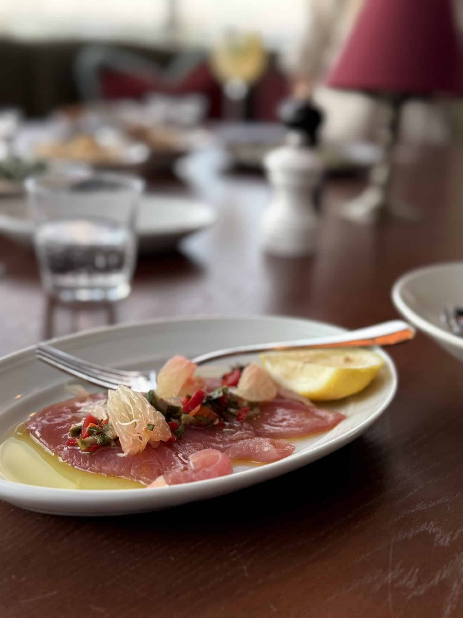 Rå tunskiver med grapefrugt, chili, urter og citronbåd på oval tallerken