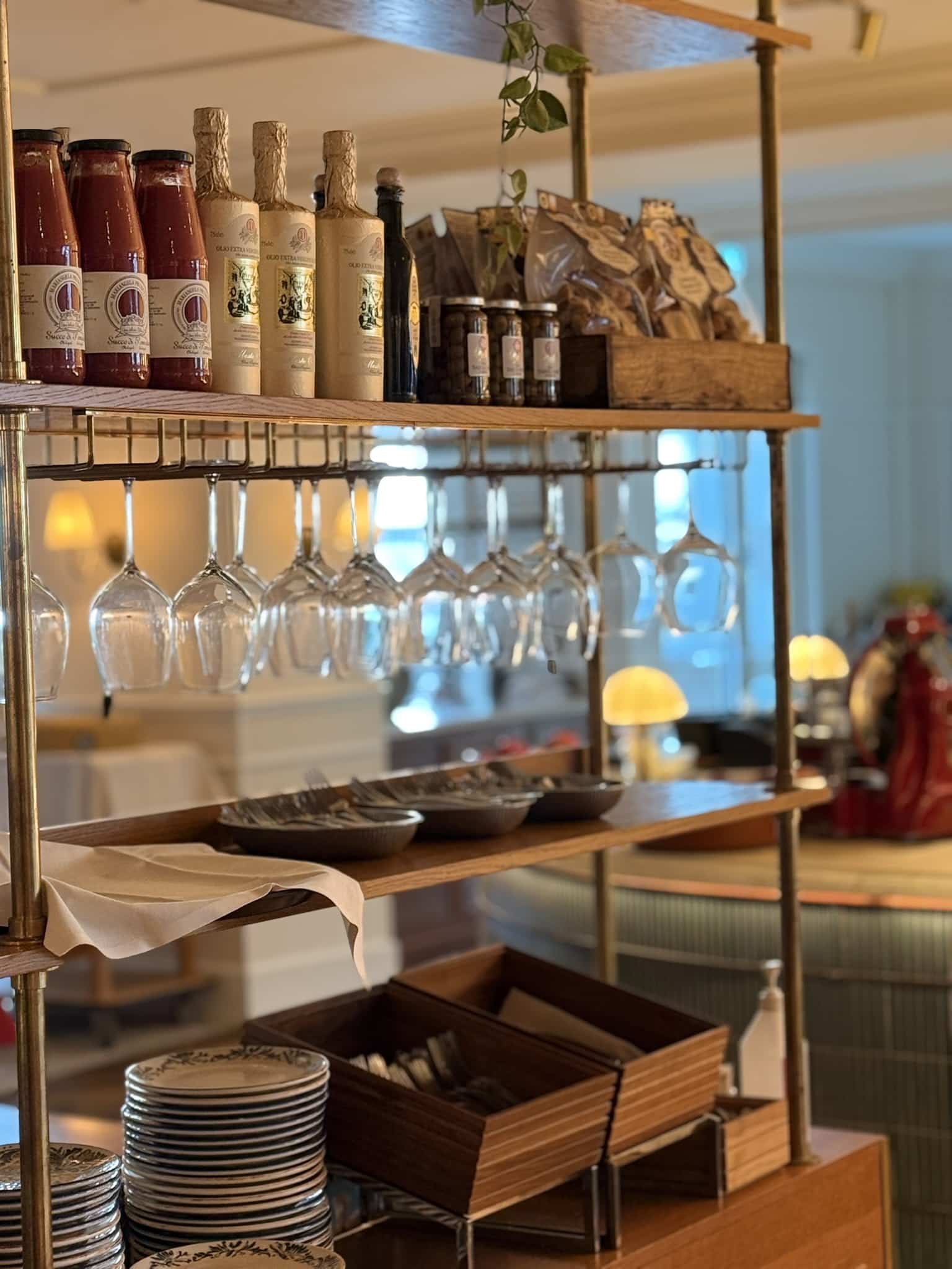 Hylde med tomatsauceflasker, olivenolie, ophængte vinglas og stablede tallerkener
