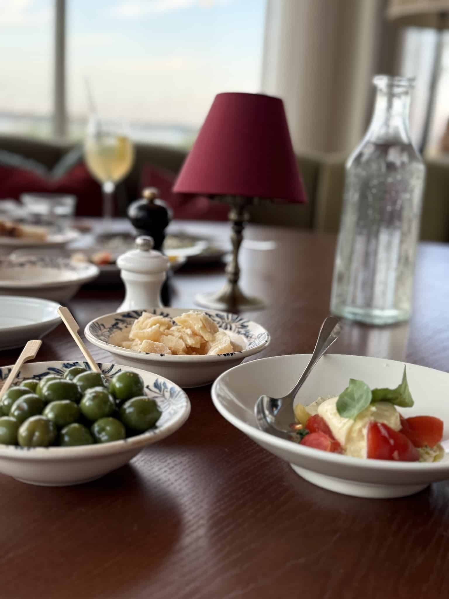 Skåle med grønne oliven, parmesanstykker og tomatsalat med burrata og basilikum