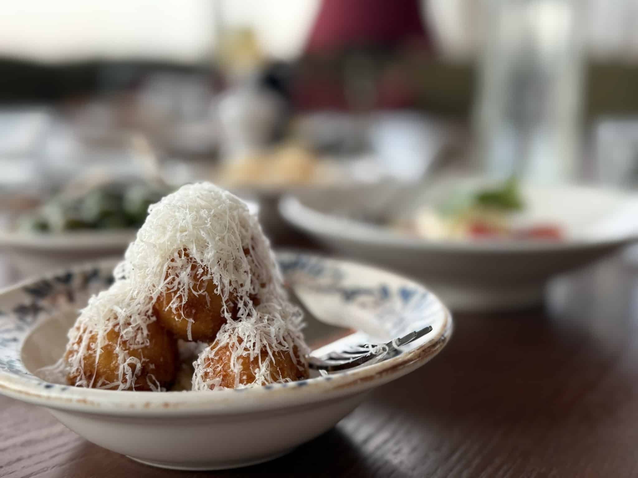 Tre friturestegte kugler dækket af revet parmesan i mønstret skål