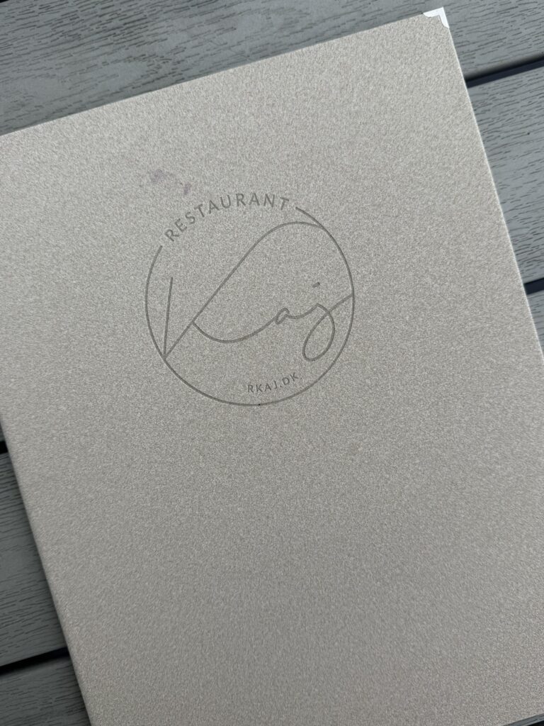 Beige menukort med Restaurant Kaj-logo på gråt træbord