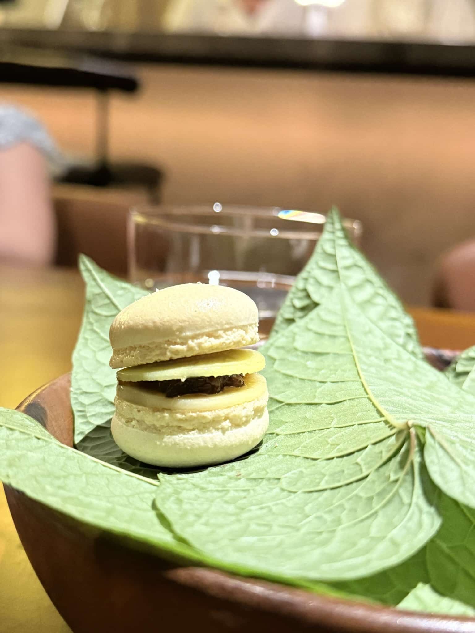Lys macaron med mørkt fyld og skiver på grønne blade i træskål