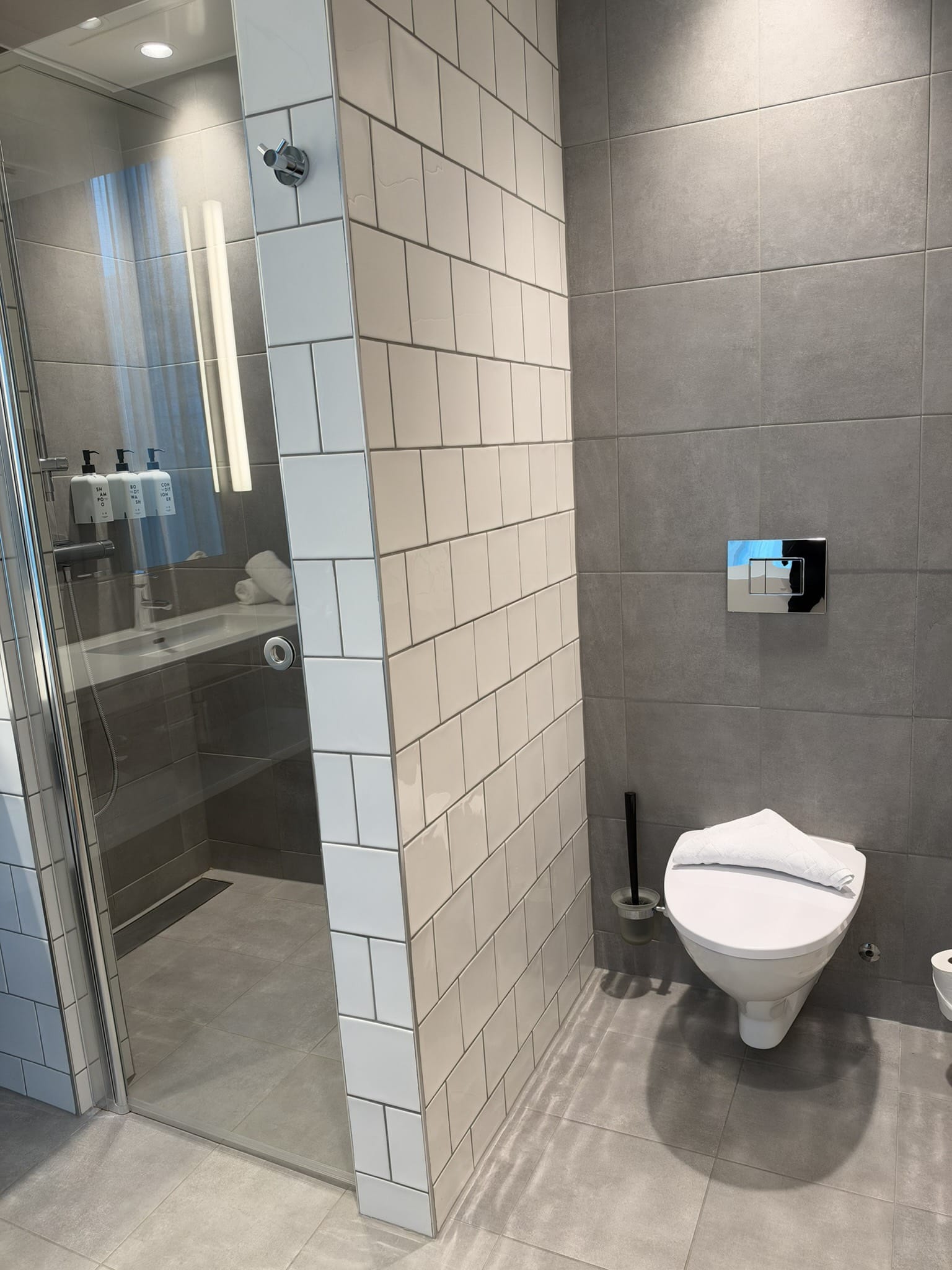 Badeværelse med glasbruseniche, hvide fliser, grå vægge og væghængt toilet