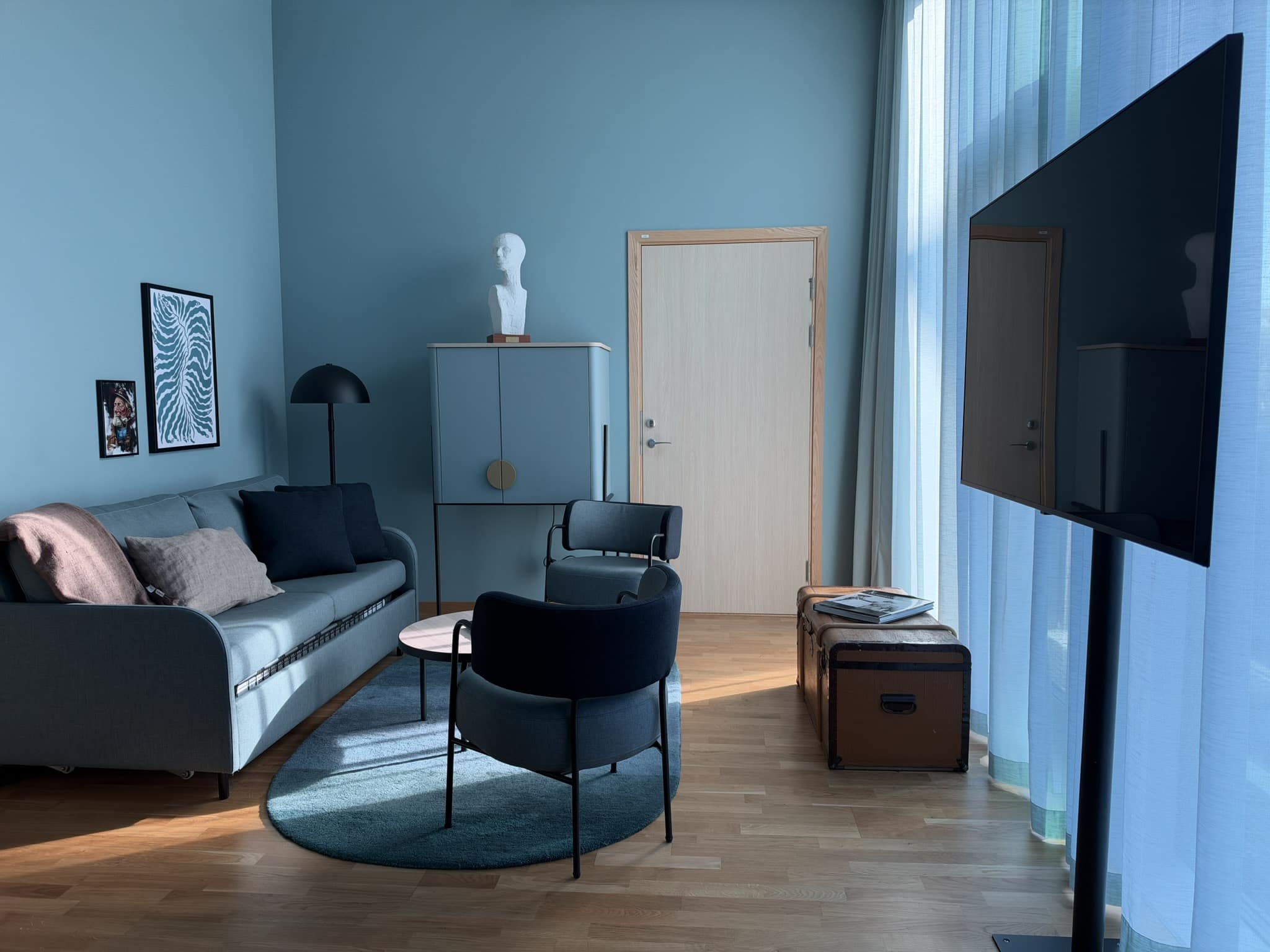 Blåmalet opholdsstue med sofa, lænestol, skab med buste, kuffert og tv