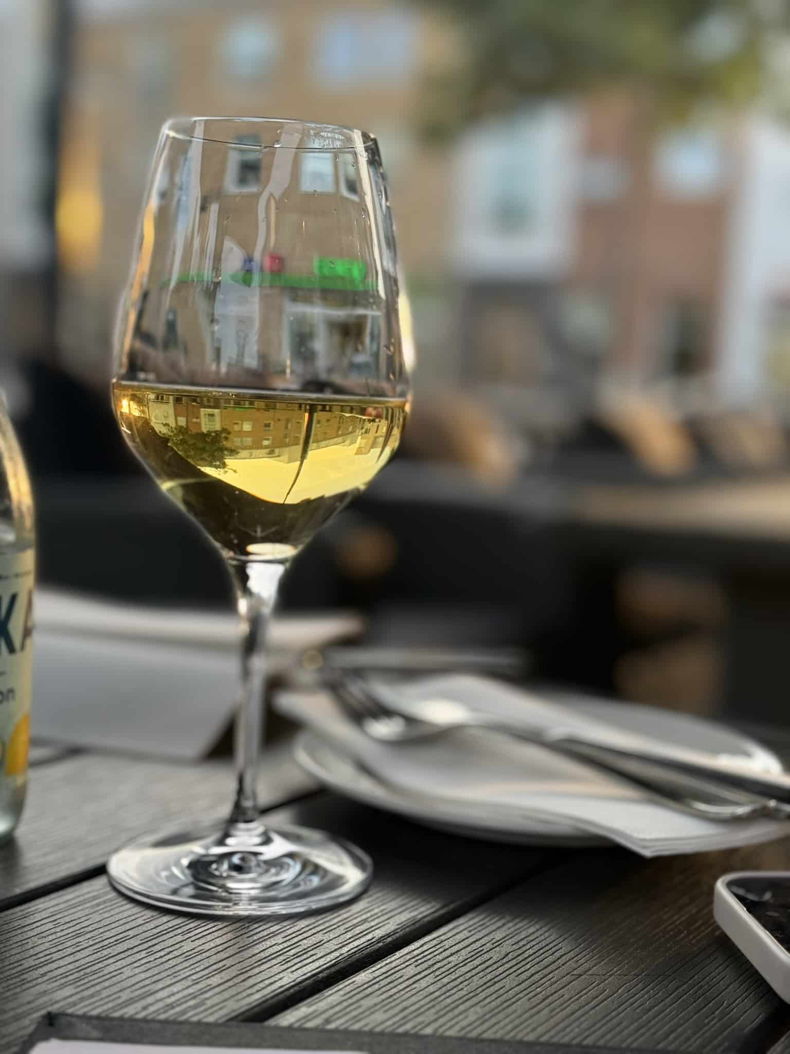 Glas hvidvin på udendørsbord med bestik og serviet bagved
