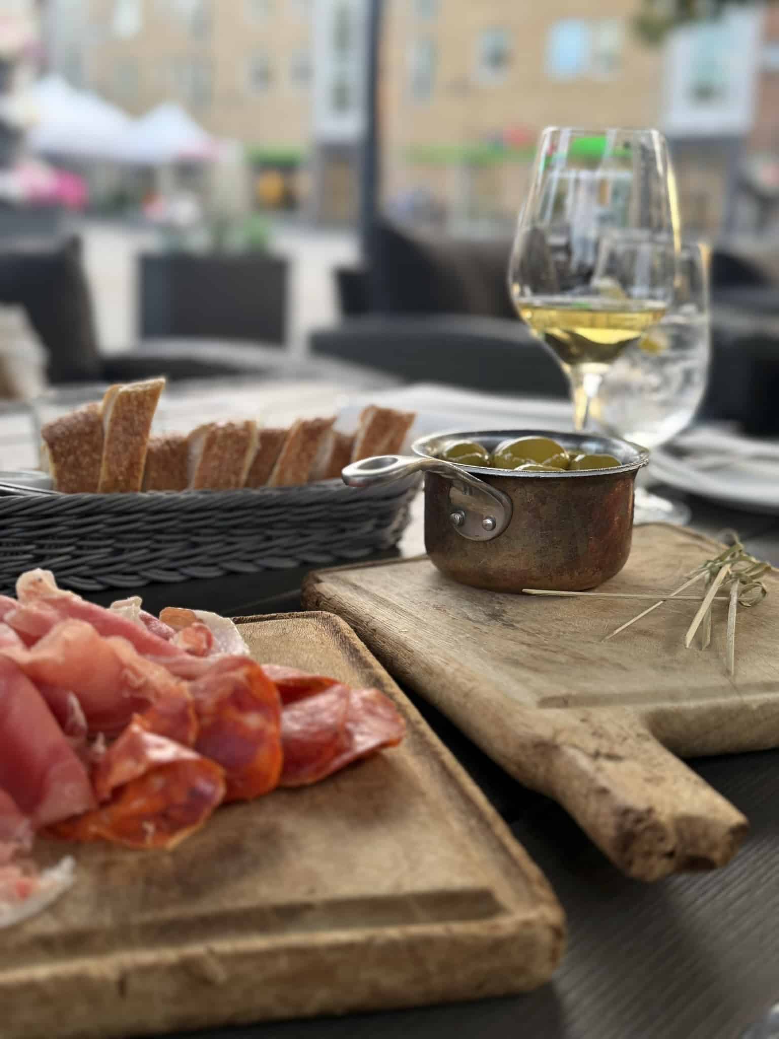 Skærebræt med skinke og chorizo, grønne oliven i kobbergryde og brødkurv