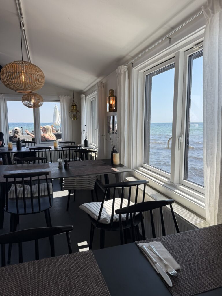 Restaurantlokale med sorte stole, borde og udsigt til havet gennem vinduer