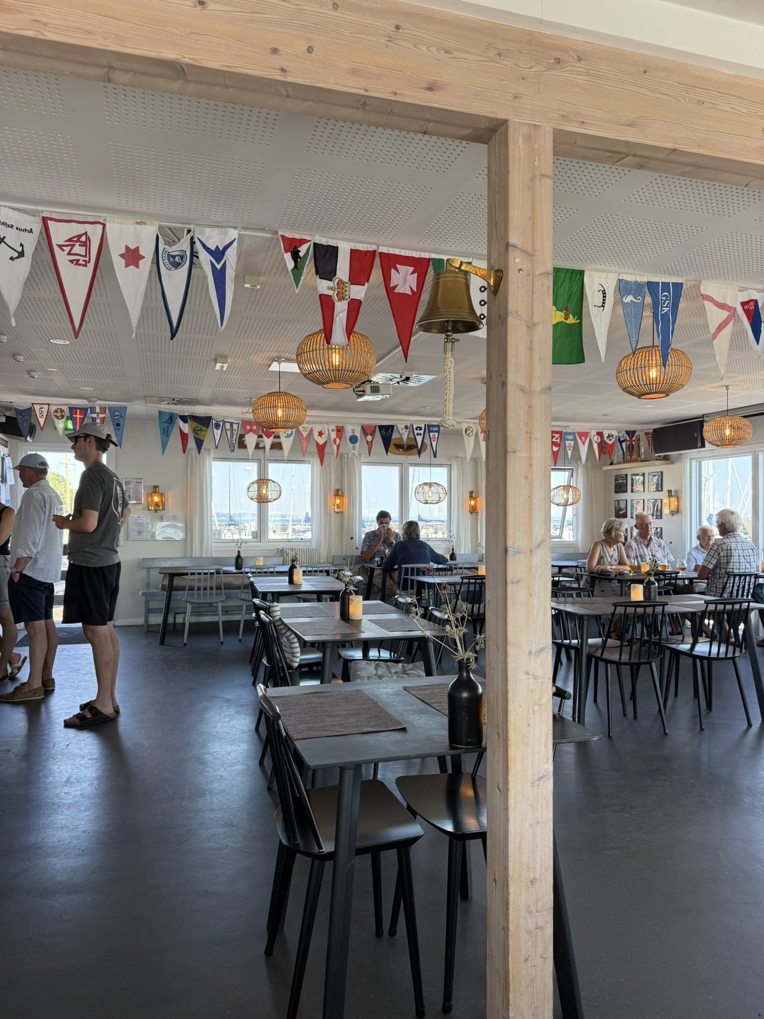 Restaurantlokale med vimpler i loftet, skibsklokke, rattanlamper og gæster