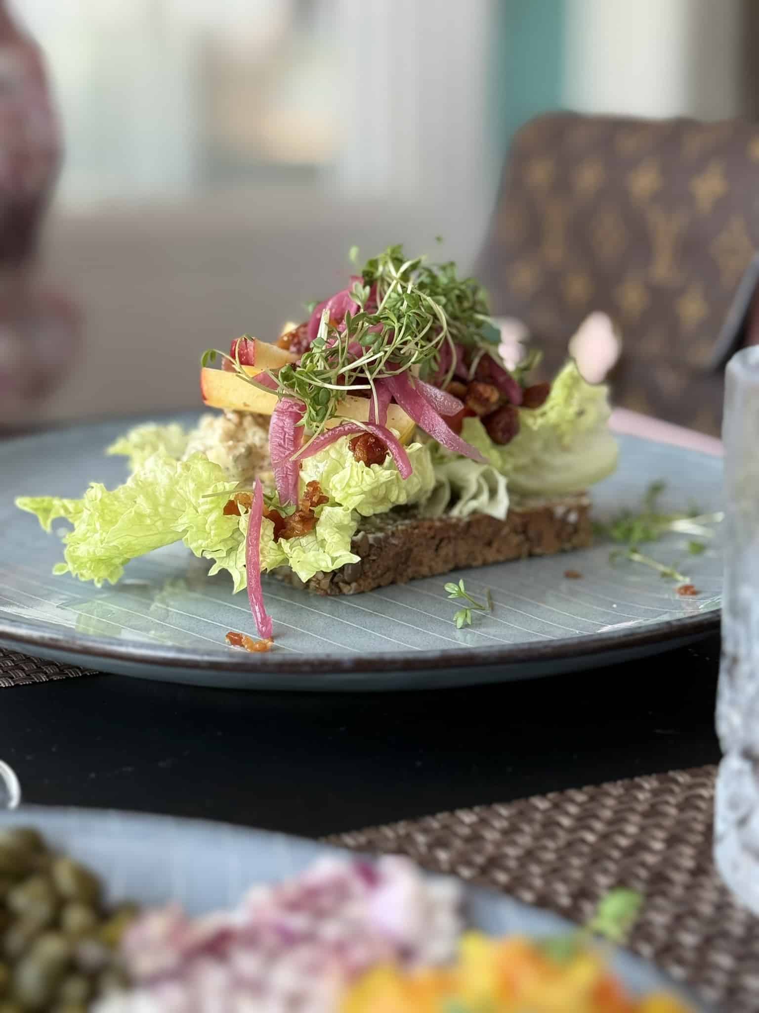 Smørrebrød på rugbrød med salat, æblestave, syltet rødløg, bacon og karse