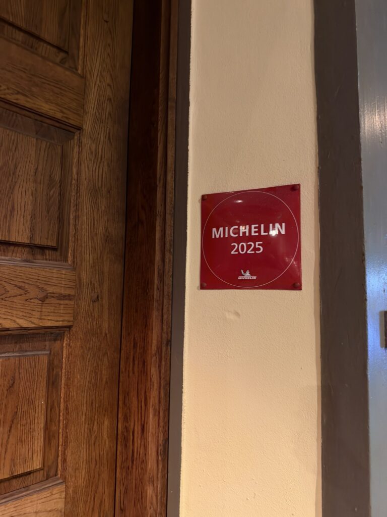 Rødt Michelin 2025-skilt på væg ved mørk trædør.