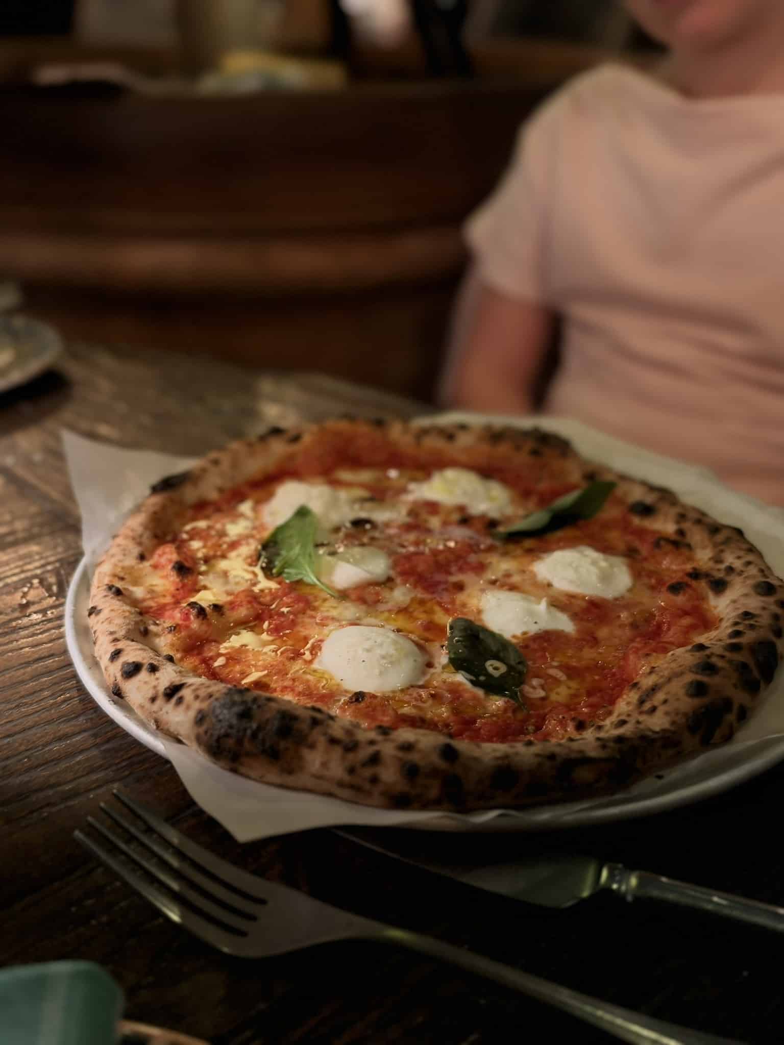 Pizza margherita med mozzarella og basilikum på hvid tallerken ved træbord.