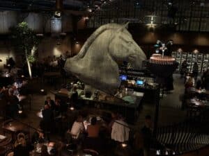 Stor hestehovedskulptur over bar med gæster ved borde nedenunder