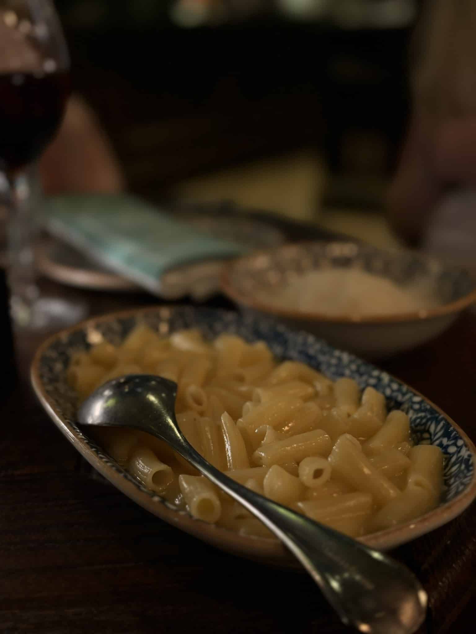 Oval skål med penne pasta i smørsauce og serveringsske