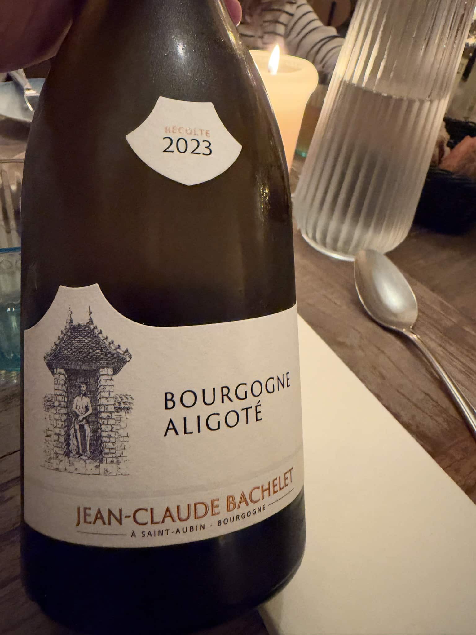 Flaske Bourgogne Aligoté 2023 fra Jean-Claude Bachelet holdt over bord med stearinlys
