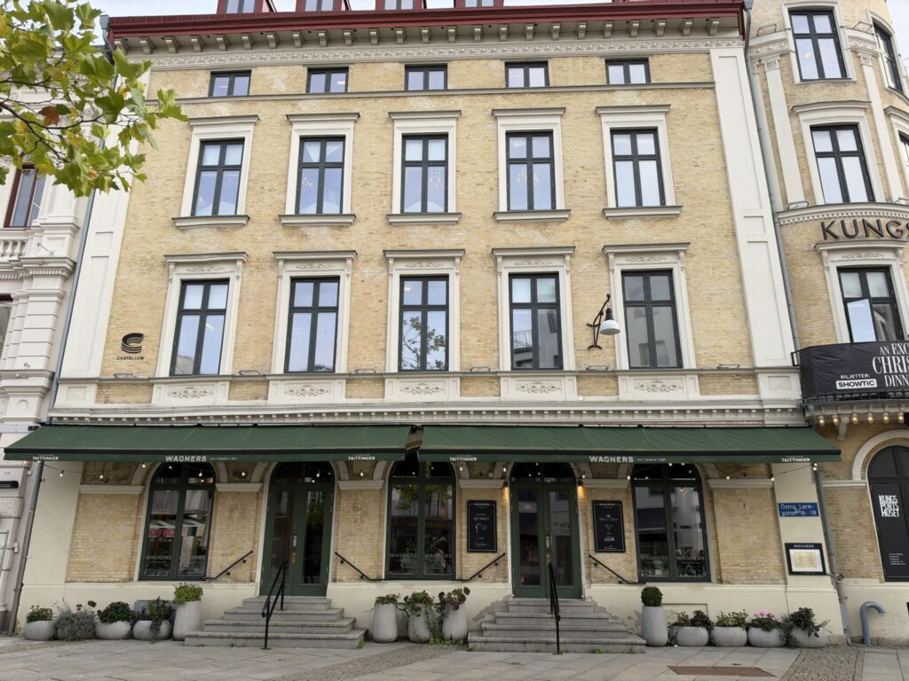 Gul murstensfacade med grønne markiser og indgang til Wagners bistro