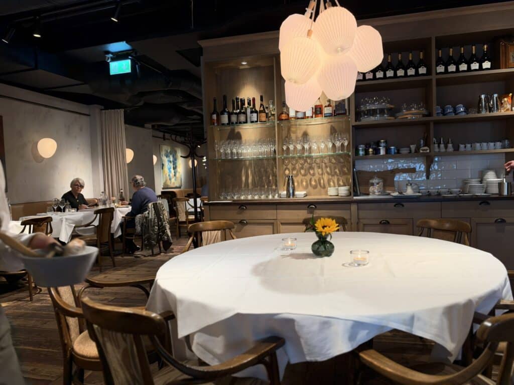 Rundt bord med hvid dug, solsikke og lampe i restaurantlokale