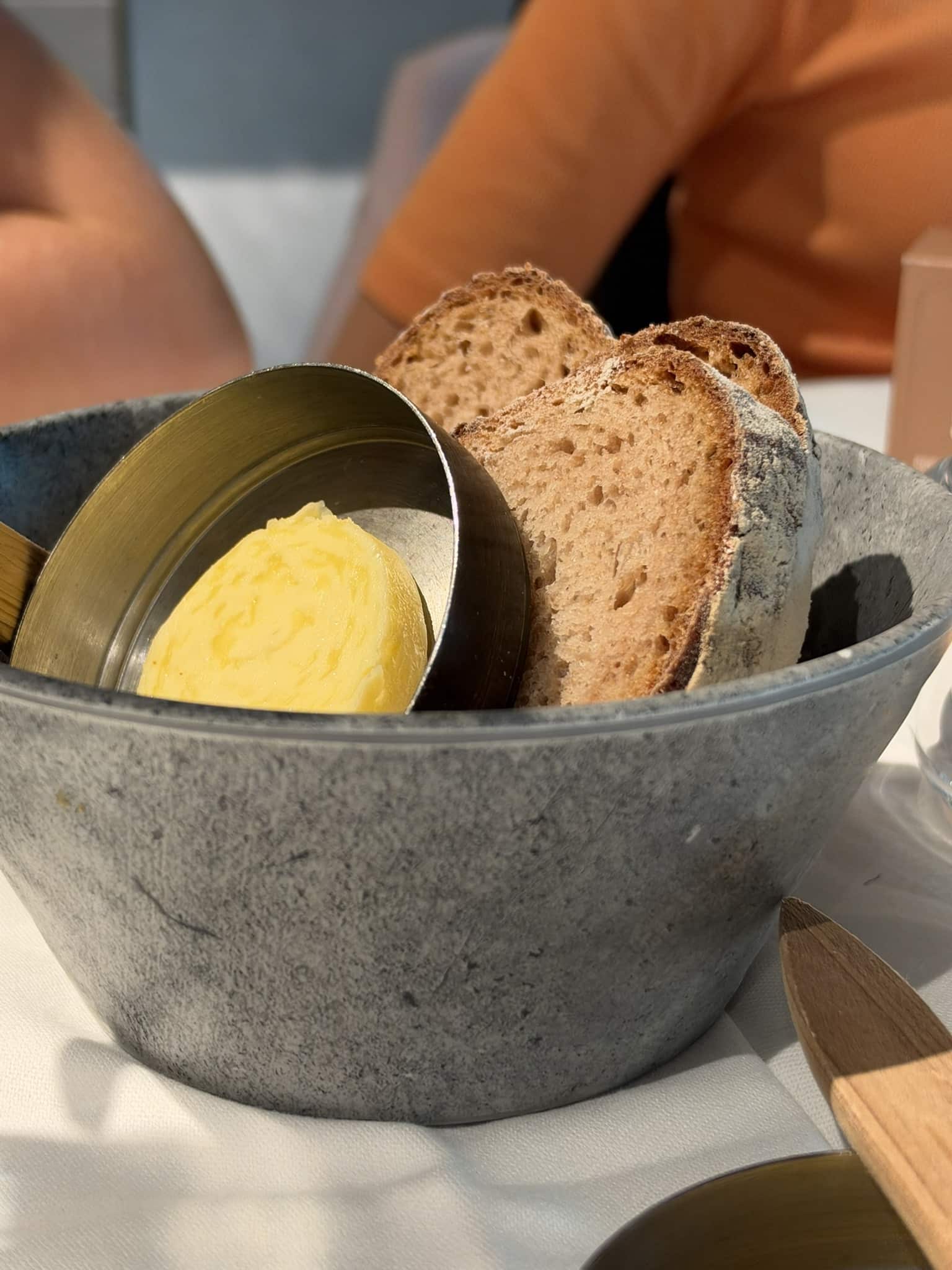 Skiver af surdejsbrød og smør i en grå stenskål på hvid dug